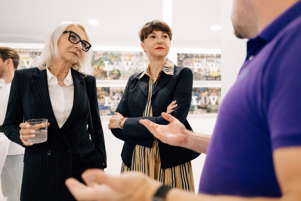 Zwei Frauen, darunter Ines Thiele-Seidel, hören einem Mann im violetten Poloshirt bei einem fokussierten Gespräch auf einem Business Networking Event aufmerksam zu.